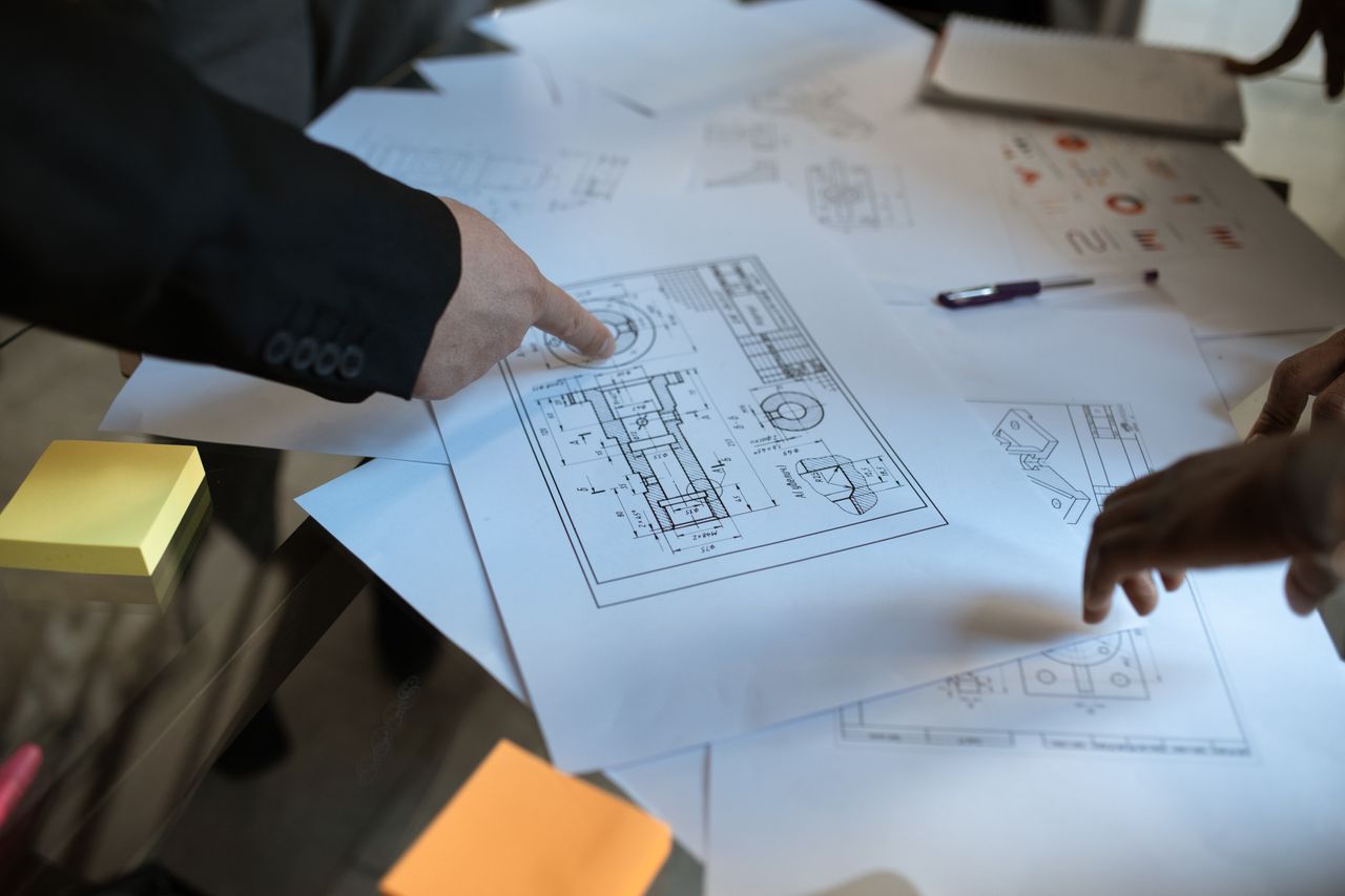 about-us-02 Engineers discussing blueprints at a workspace, focusing on teamwork and architecture design.